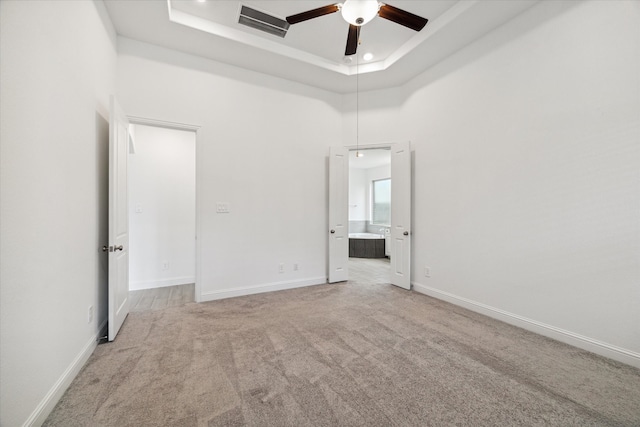 unfurnished bedroom with a tray ceiling, light colored carpet, a towering ceiling, and ceiling fan