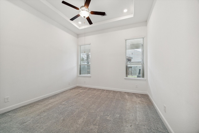 empty room featuring a tray ceiling, ceiling fan, and light colored carpet