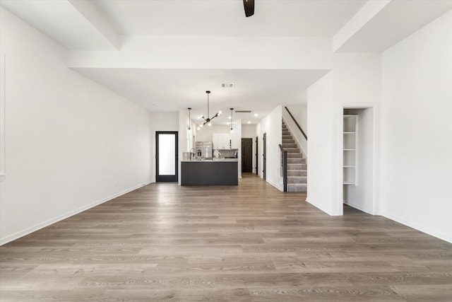 unfurnished living room featuring ceiling fan with notable chandelier, wood-type flooring, and sink