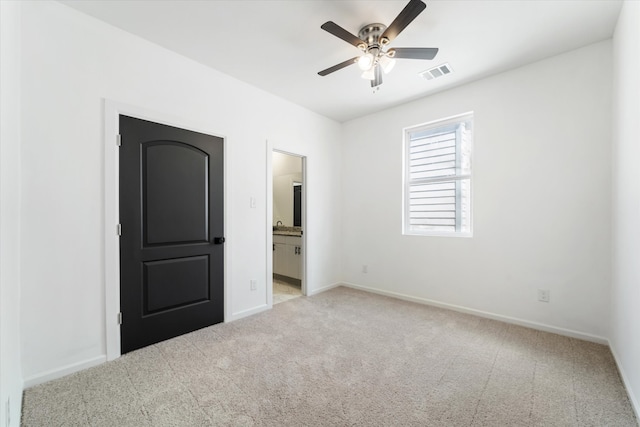 unfurnished bedroom featuring ceiling fan, light carpet, and ensuite bath