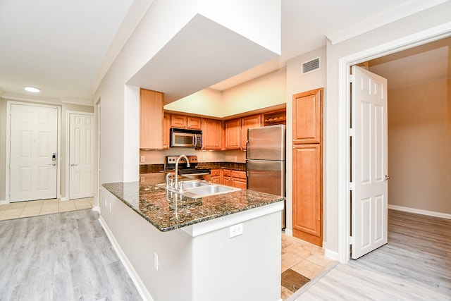 kitchen with light wood-type flooring, dark stone countertops, crown molding, kitchen peninsula, and appliances with stainless steel finishes