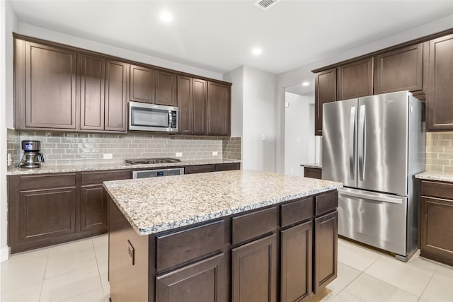 kitchen featuring tasteful backsplash, appliances with stainless steel finishes, a kitchen island, dark brown cabinets, and light tile patterned floors