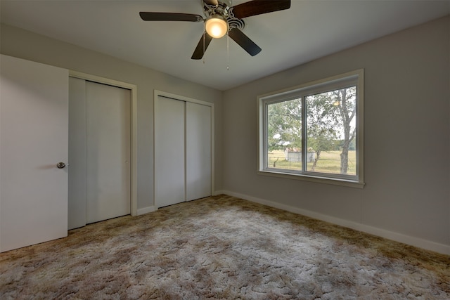 unfurnished bedroom with multiple closets, light colored carpet, and ceiling fan