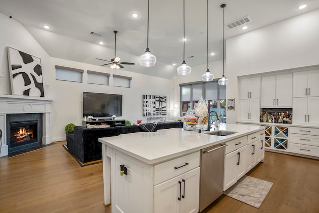 kitchen featuring white cabinets, a center island with sink, ceiling fan, stainless steel dishwasher, and wood-type flooring