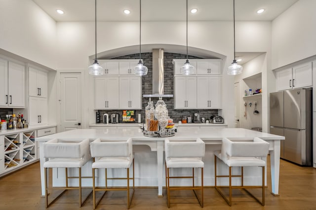 kitchen featuring a spacious island, hanging light fixtures, wall chimney range hood, and stainless steel refrigerator