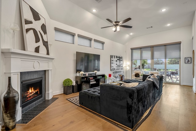 living room featuring lofted ceiling, a tiled fireplace, light wood-type flooring, and ceiling fan