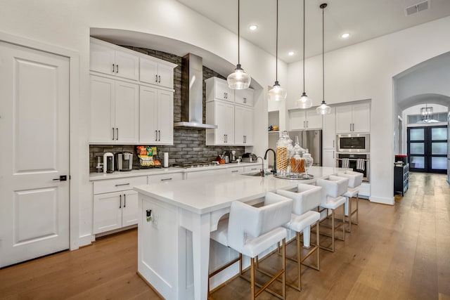 kitchen with white cabinets, an island with sink, a kitchen bar, light hardwood / wood-style flooring, and wall chimney exhaust hood