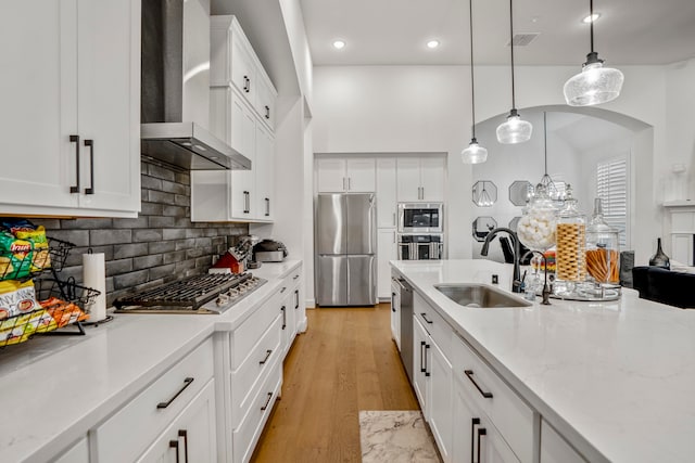 kitchen featuring appliances with stainless steel finishes, white cabinetry, light hardwood / wood-style flooring, wall chimney exhaust hood, and decorative light fixtures