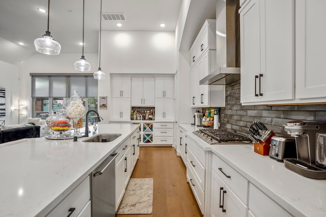 kitchen with wall chimney range hood, white cabinets, light stone counters, sink, and decorative light fixtures