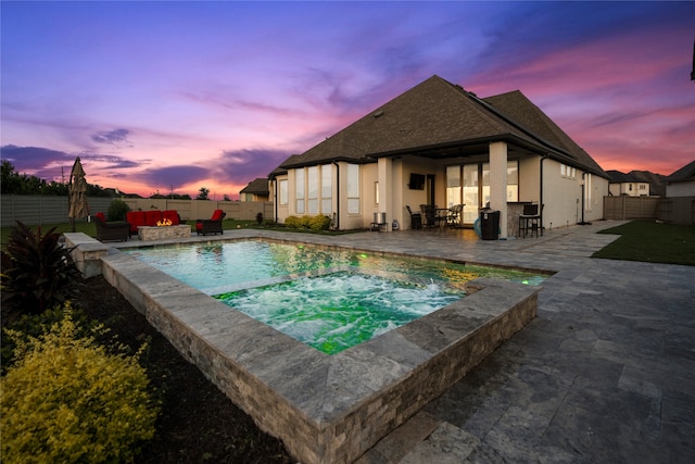 pool at dusk featuring a patio and an in ground hot tub