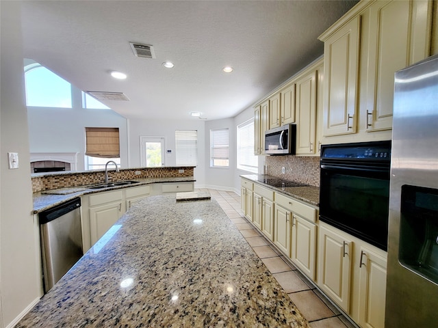 kitchen with stone counters, black appliances, sink, and cream cabinetry