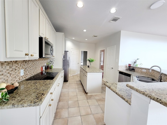 kitchen with light stone countertops, sink, white cabinetry, stainless steel appliances, and a center island with sink