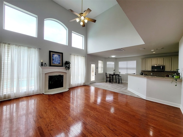 unfurnished living room with light hardwood / wood-style floors, a high ceiling, and ceiling fan