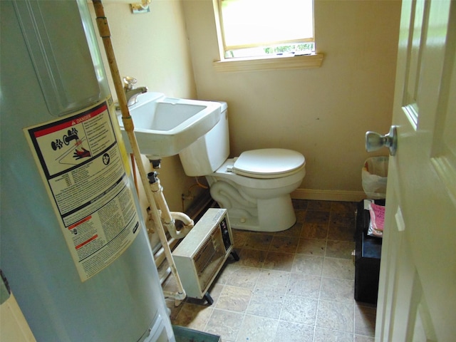 half bath featuring toilet, baseboards, water heater, and a sink