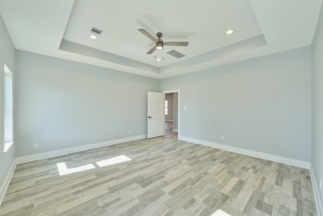 empty room with ceiling fan, a raised ceiling, and light hardwood / wood-style flooring