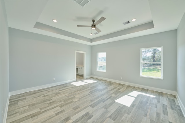 unfurnished room with a raised ceiling, ceiling fan, and light hardwood / wood-style floors