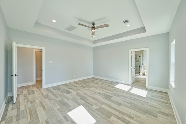 spare room featuring ceiling fan, light wood-type flooring, and a tray ceiling