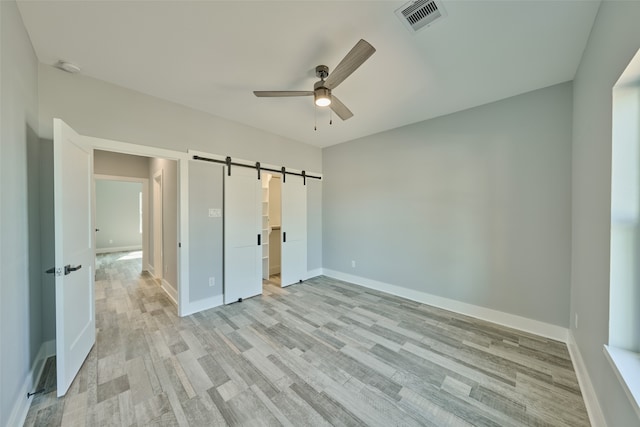 unfurnished bedroom with a barn door, ceiling fan, and light hardwood / wood-style flooring