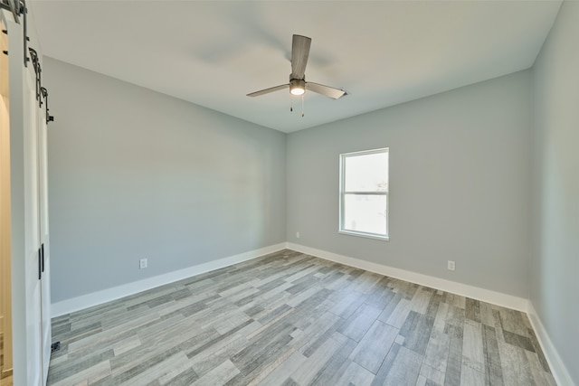 empty room with light hardwood / wood-style flooring, ceiling fan, and a barn door