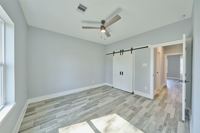 unfurnished bedroom with a barn door, a closet, ceiling fan, and light wood-type flooring