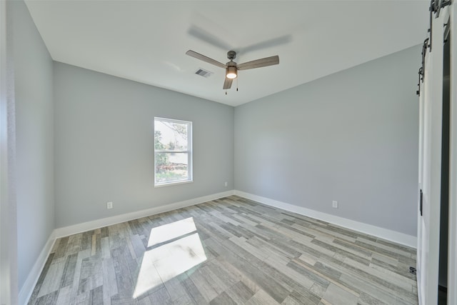 empty room featuring a barn door, ceiling fan, and light hardwood / wood-style flooring