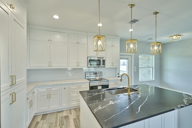 kitchen featuring a kitchen island with sink, appliances with stainless steel finishes, white cabinetry, and decorative light fixtures