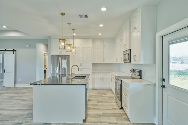 kitchen featuring white cabinets, a barn door, stainless steel appliances, sink, and an island with sink