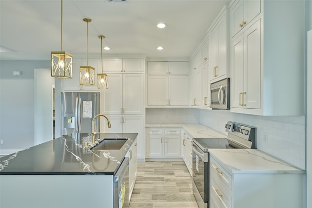 kitchen featuring white cabinets, decorative light fixtures, stainless steel appliances, sink, and a center island with sink