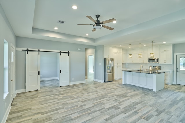 kitchen featuring decorative light fixtures, a barn door, ceiling fan, appliances with stainless steel finishes, and white cabinets