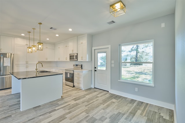 kitchen featuring sink, stainless steel appliances, white cabinets, and a center island with sink