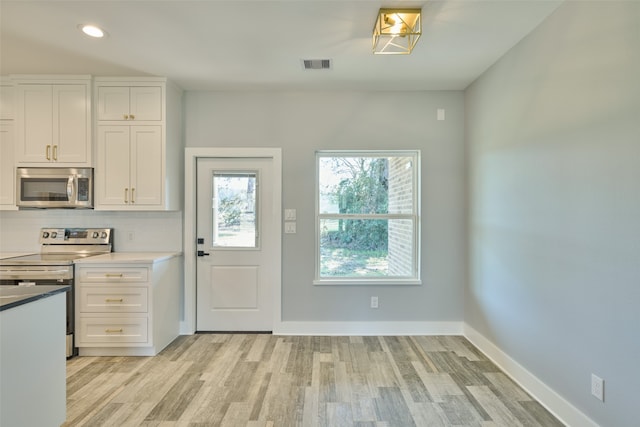 interior space featuring tasteful backsplash, stainless steel appliances, white cabinetry, and light hardwood / wood-style flooring