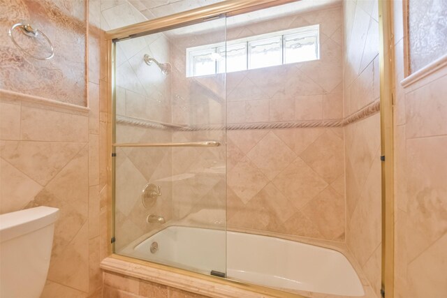 bathroom featuring toilet and shower / bath combination with glass door