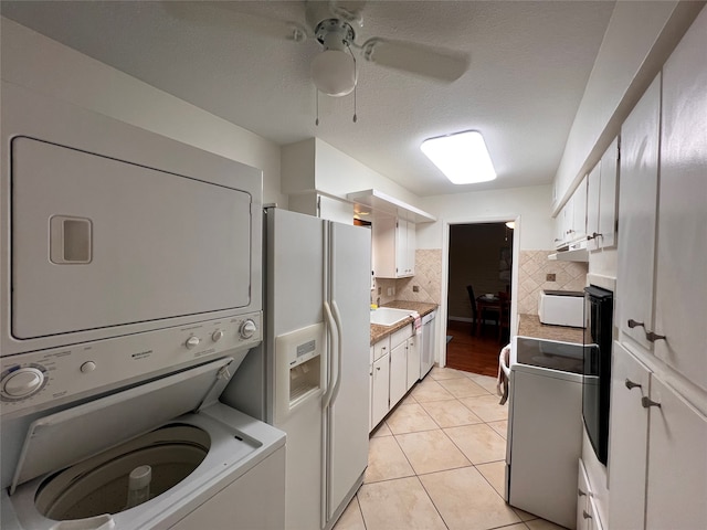 clothes washing area with a textured ceiling, ceiling fan, stacked washer / dryer, and light tile patterned flooring