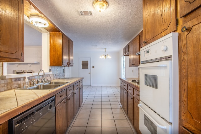 kitchen featuring dishwasher, a notable chandelier, light tile patterned floors, sink, and double oven