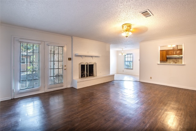 unfurnished living room featuring a textured ceiling, a brick fireplace, a chandelier, dark hardwood / wood-style floors, and ornamental molding