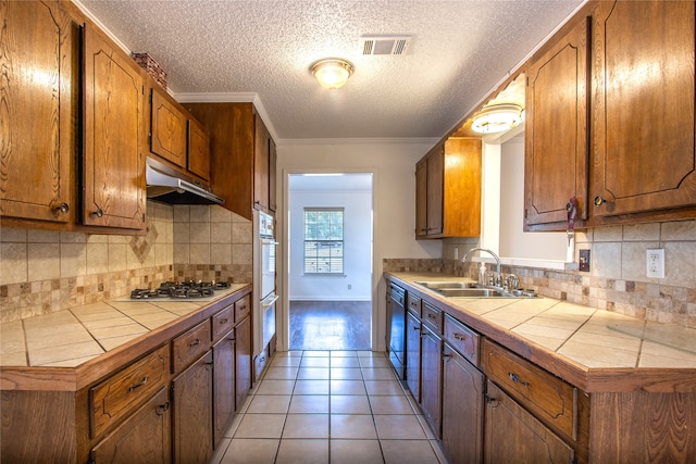 kitchen featuring light wood-type flooring, stainless steel gas stovetop, tile counters, and ornamental molding