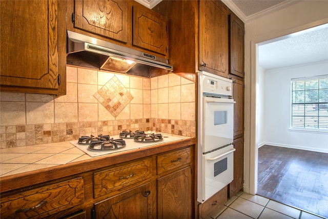 kitchen with white appliances, wood-type flooring, tasteful backsplash, tile counters, and ornamental molding