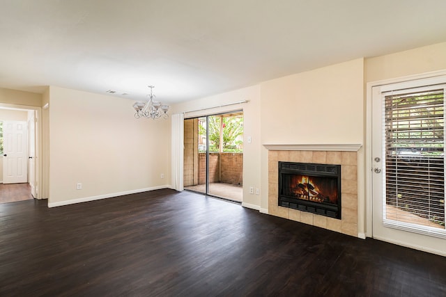 unfurnished living room with dark hardwood / wood-style floors, a tile fireplace, and a chandelier