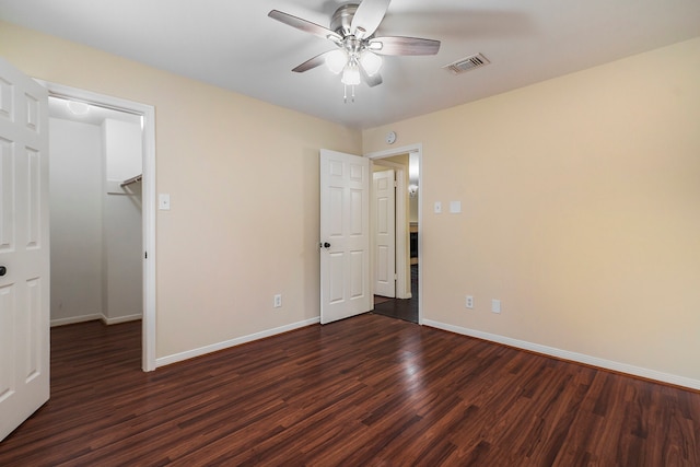 unfurnished bedroom with a walk in closet, a closet, ceiling fan, and dark wood-type flooring