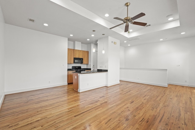 kitchen featuring ceiling fan, pendant lighting, kitchen peninsula, black appliances, and light wood-type flooring