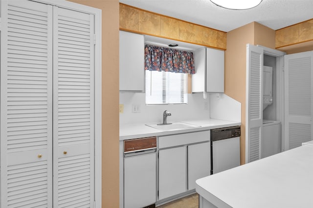 kitchen featuring stacked washer and dryer, a textured ceiling, sink, stainless steel dishwasher, and white cabinets