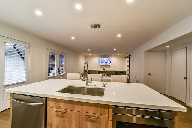 kitchen featuring a center island with sink, a barn door, sink, and appliances with stainless steel finishes