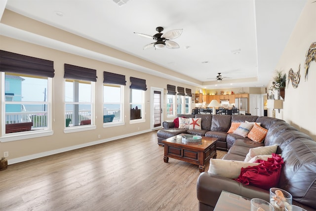 living room featuring a tray ceiling, ceiling fan, and light wood-type flooring