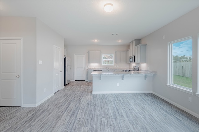 kitchen with light hardwood / wood-style flooring, stainless steel appliances, kitchen peninsula, light stone countertops, and a breakfast bar