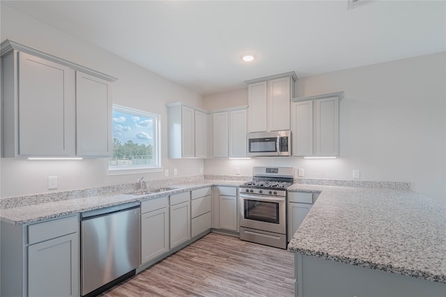 kitchen featuring gray cabinetry, light wood-type flooring, appliances with stainless steel finishes, light stone countertops, and sink