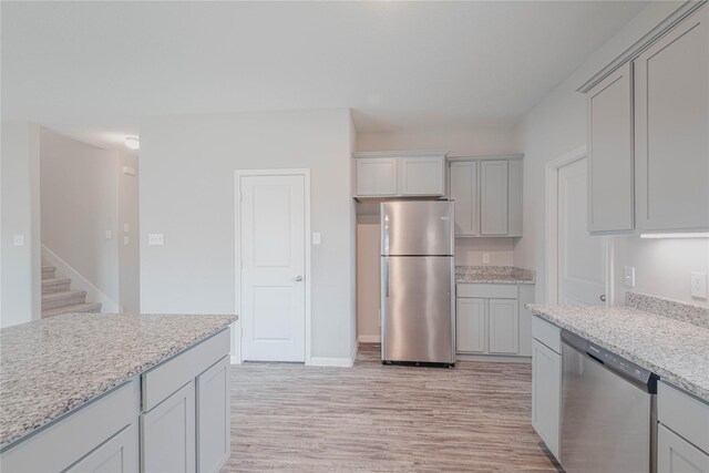 kitchen with gray cabinets, light stone countertops, stainless steel appliances, and light hardwood / wood-style flooring