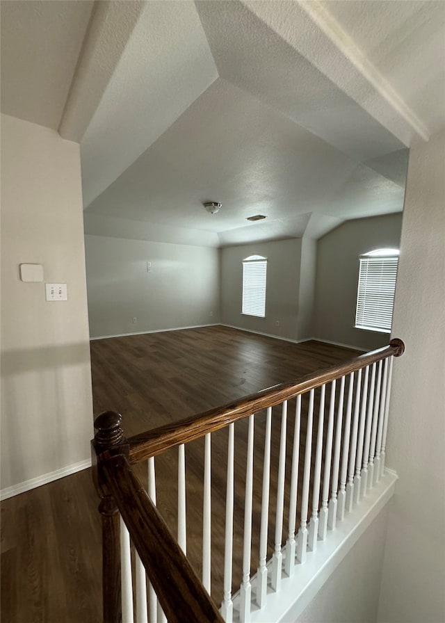 hallway with hardwood / wood-style floors, a textured ceiling, and vaulted ceiling