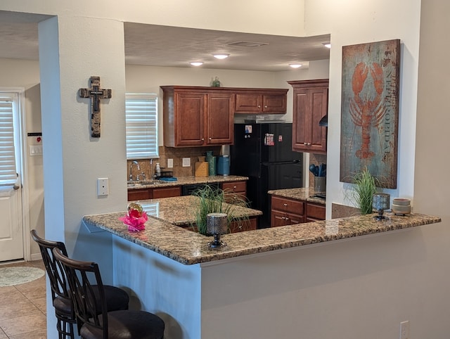 kitchen featuring kitchen peninsula, decorative backsplash, black fridge, and dark stone counters