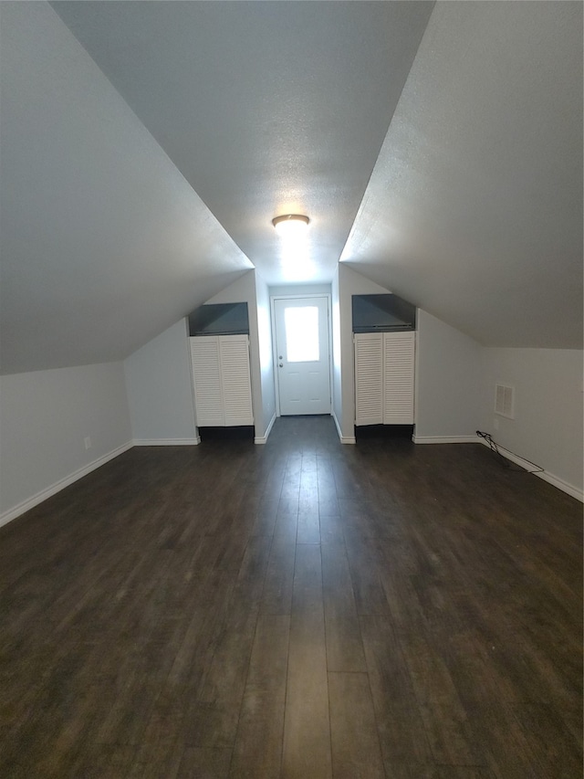 additional living space with lofted ceiling, dark hardwood / wood-style flooring, and a textured ceiling