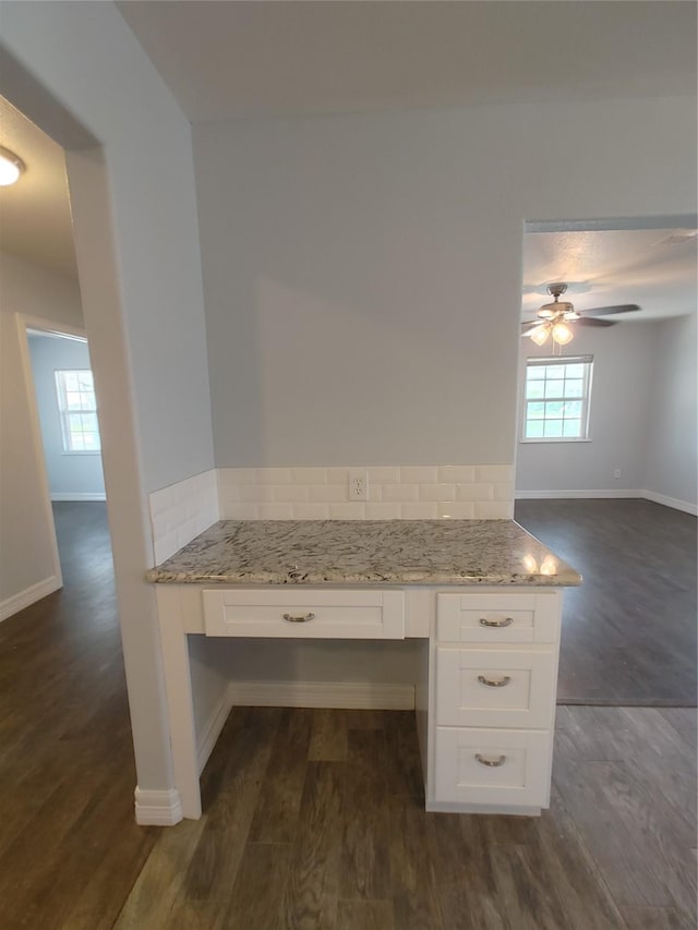 kitchen featuring built in desk, baseboards, white cabinets, light stone countertops, and dark wood-type flooring